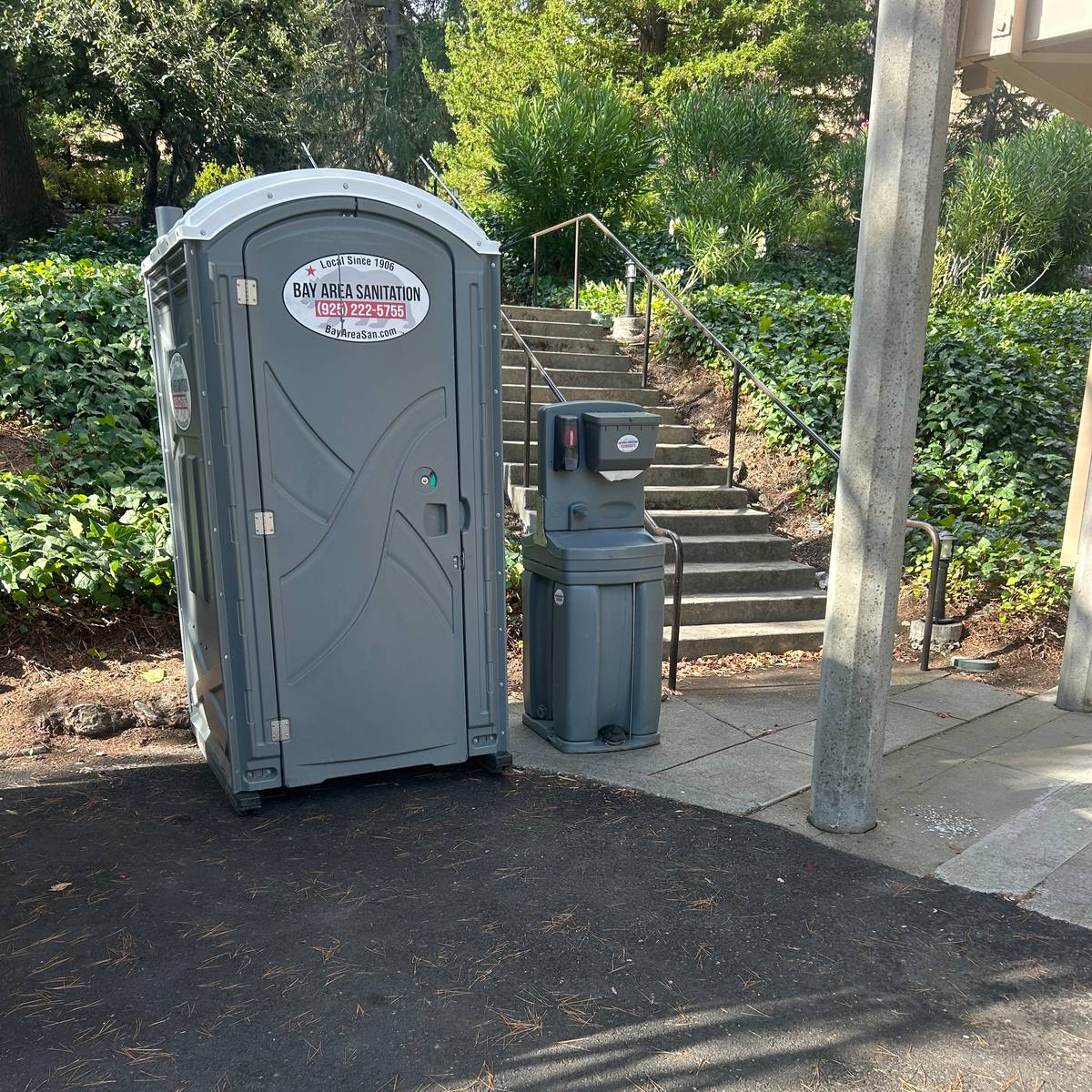 Porta potty with a freestanding hand wash station beside outdoor stairs, available for Belvedere rentals