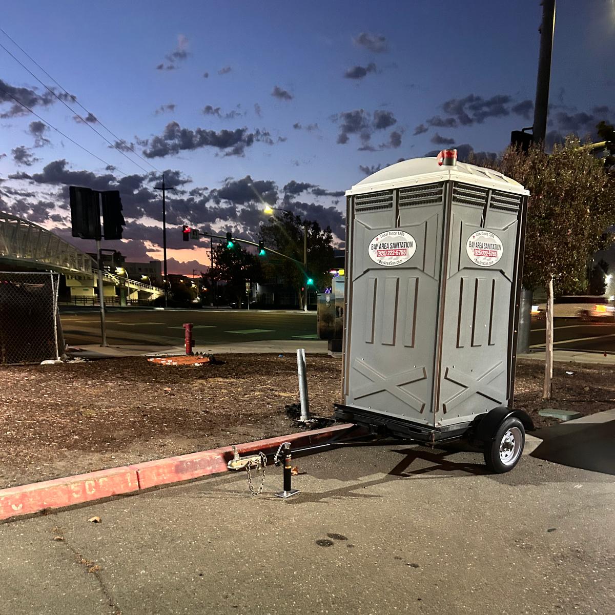 Trailer-mounted porta potty parked at a curb at dusk, available for rent in Cordelia