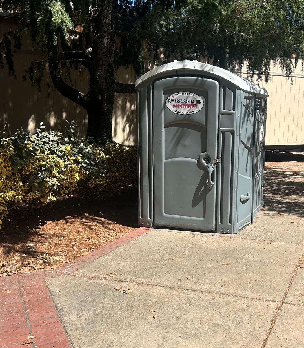 Wide-format Bay Area Sanitation portable restroom on a shaded sidewalk, available in Discovery Bay