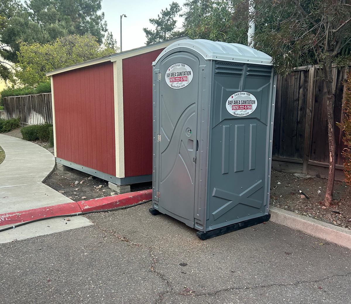 Bay Area Sanitation porta potty beside a red storage shed, available in Marin City