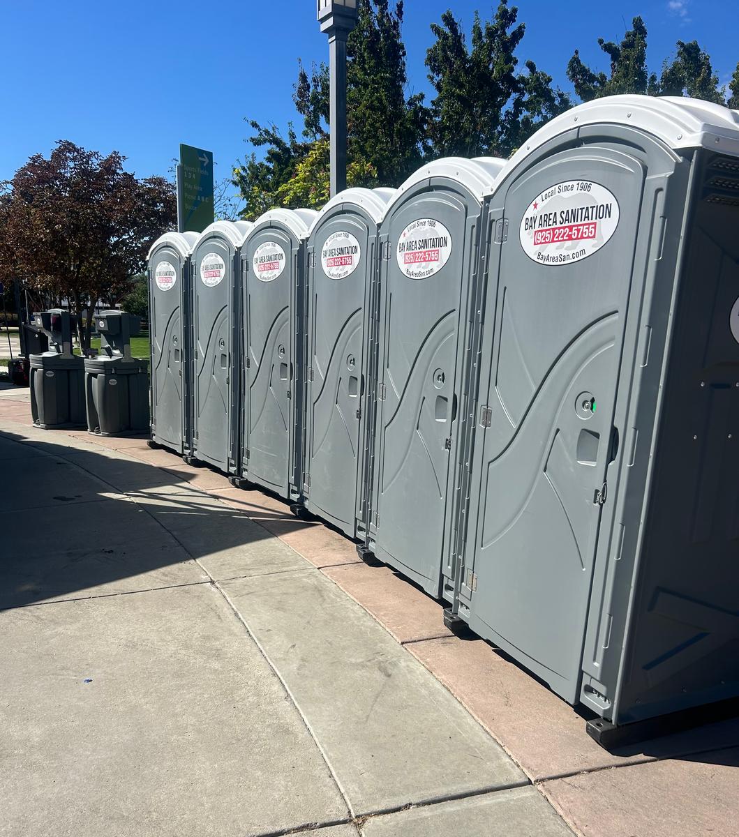 Row of six standard portable toilets on a sidewalk, available for Blackhawk events