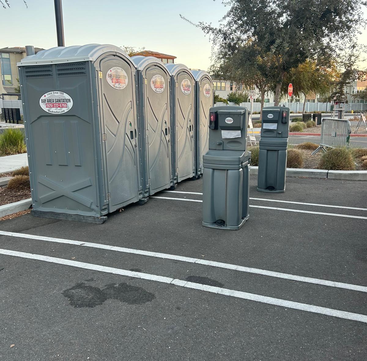 Four portable toilets and two hand wash stations in a parking lot, available in Crockett