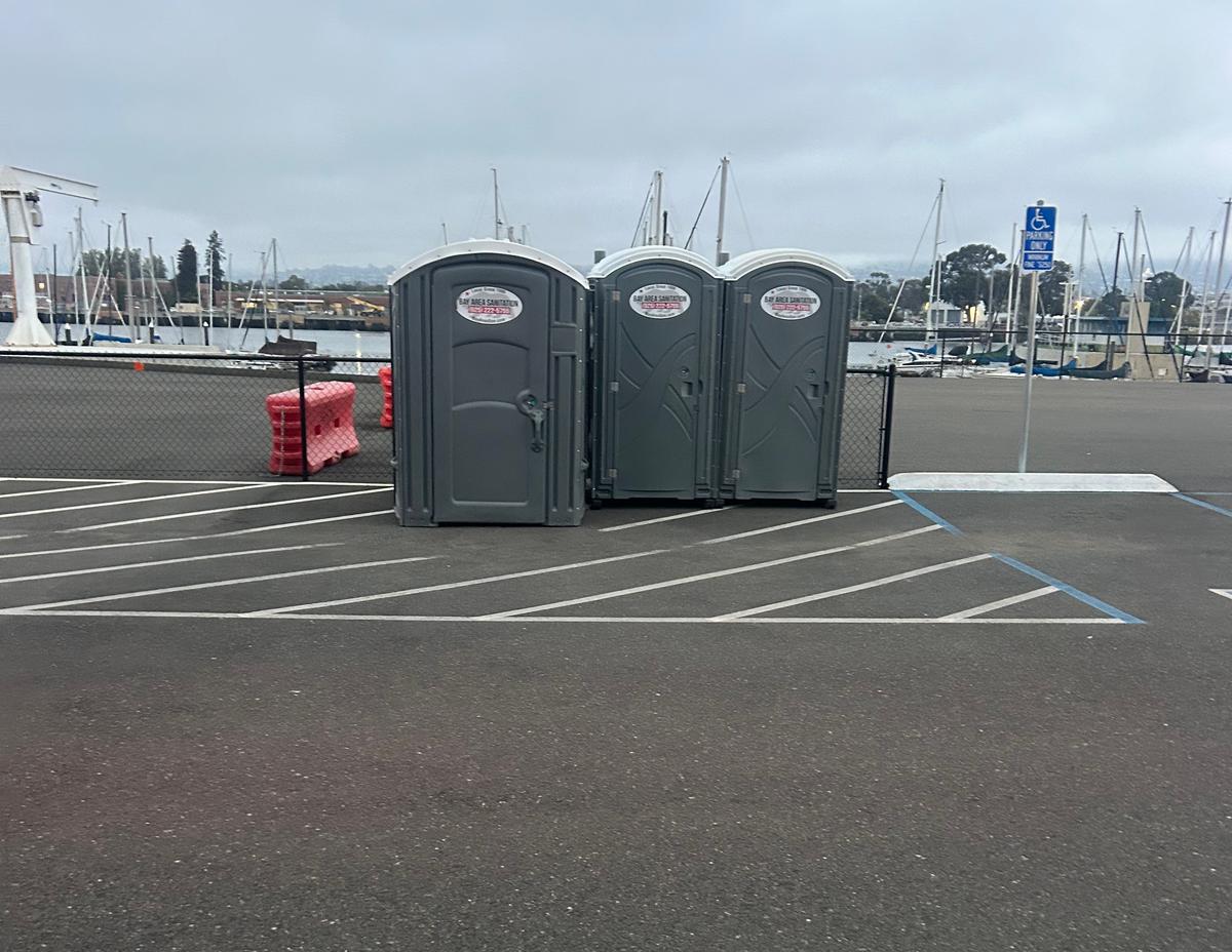 Three portable toilets in a waterfront marina parking lot, available for Belvedere events