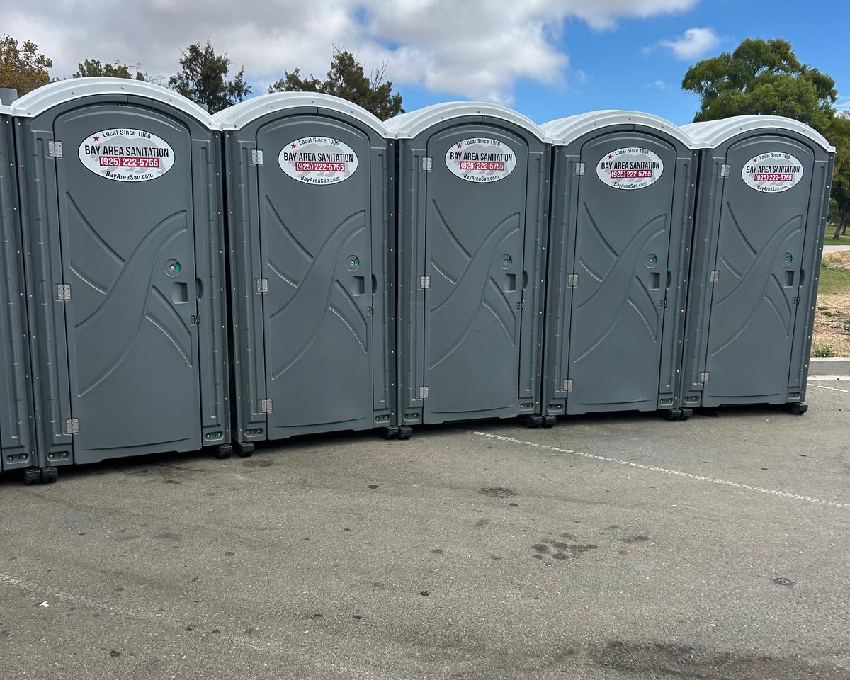 Five standard portable toilets lined up in a parking lot, available in Cordelia
