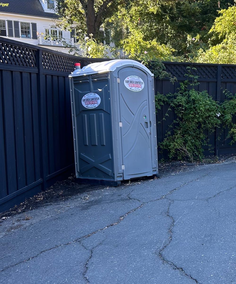 Bay Area Sanitation porta potty against a wood fence, available in Suisun City