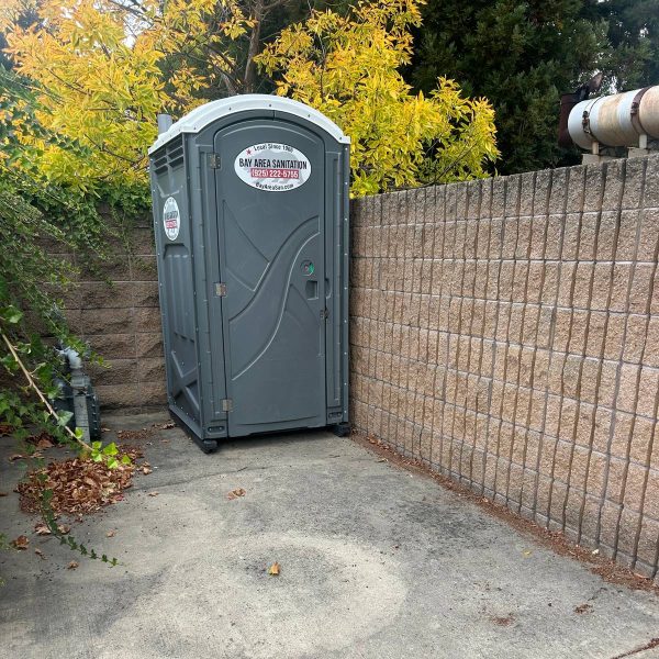 Standard porta potty placed against a block wall, available for Crockett commercial sites