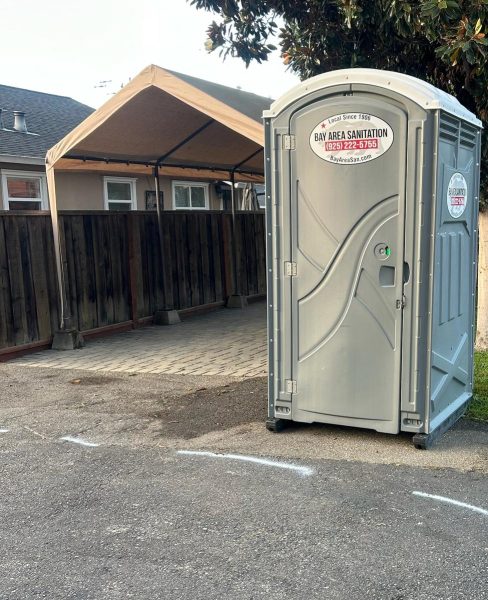 Standard porta potty at the edge of an asphalt driveway, available in Marin City